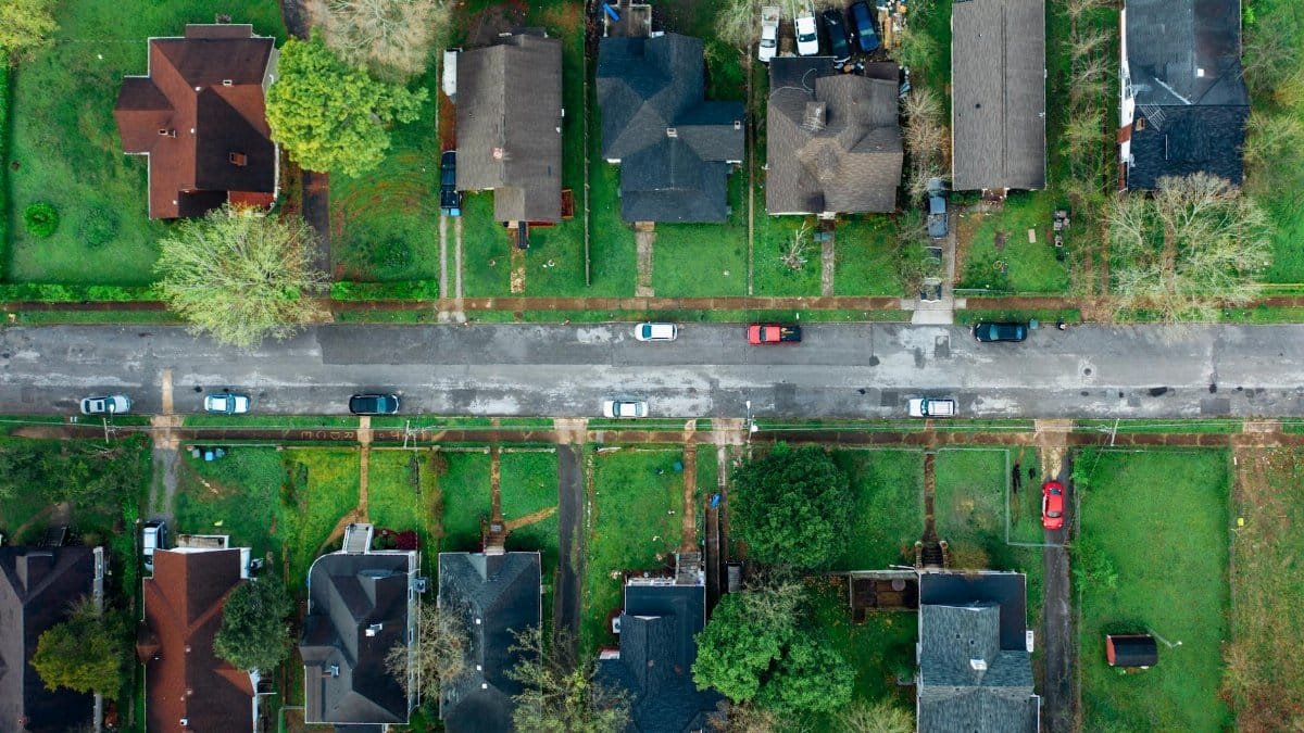 High-angle aerial shot of a suburban neighborhood street lined with houses and cars.