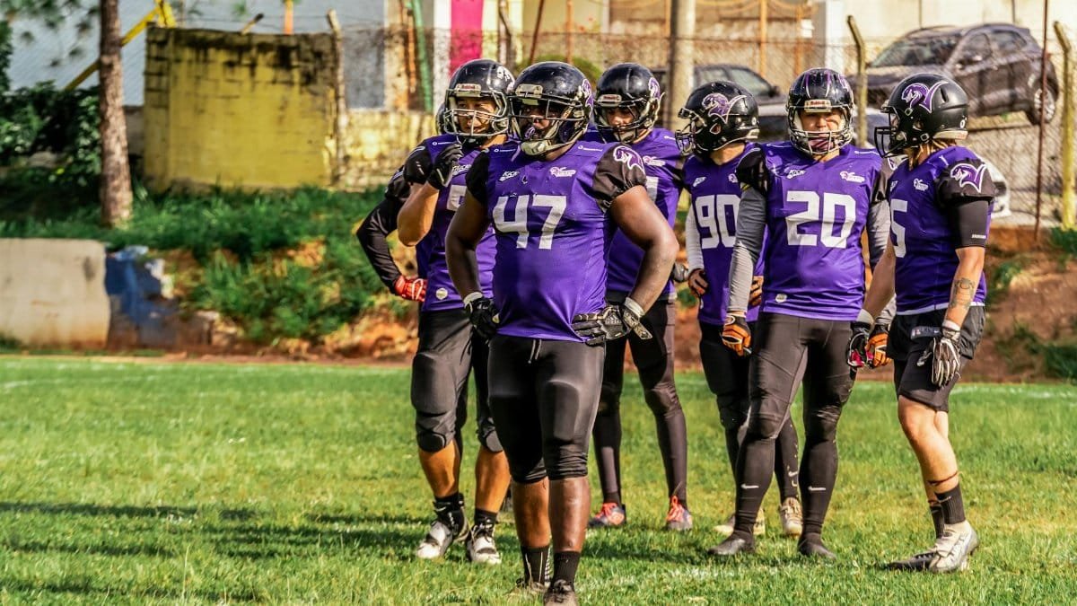 Group of American football players in purple uniforms on the field, ready for a match.