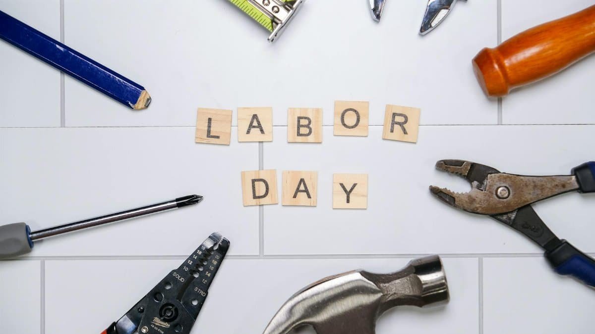 Top view of various tools with Labor Day text on white tiles, signifying the holiday and work.