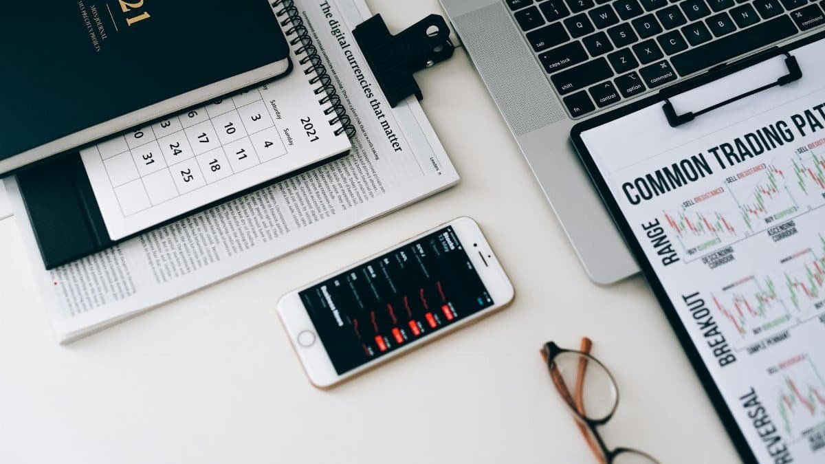Home office desk featuring trading charts, smartphone, and laptop for financial analysis.