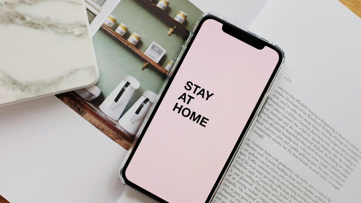 From above of modern cellphone with pale pink screen and STAY AT HOME inscription put on open magazine in apartment during COVID 19 pandemic