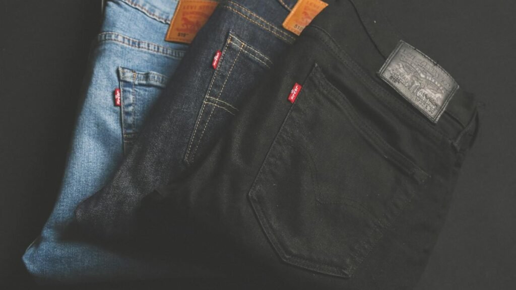 A stack of blue, dark, and black denim jeans folded on a dark surface.