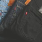A stack of blue, dark, and black denim jeans folded on a dark surface.