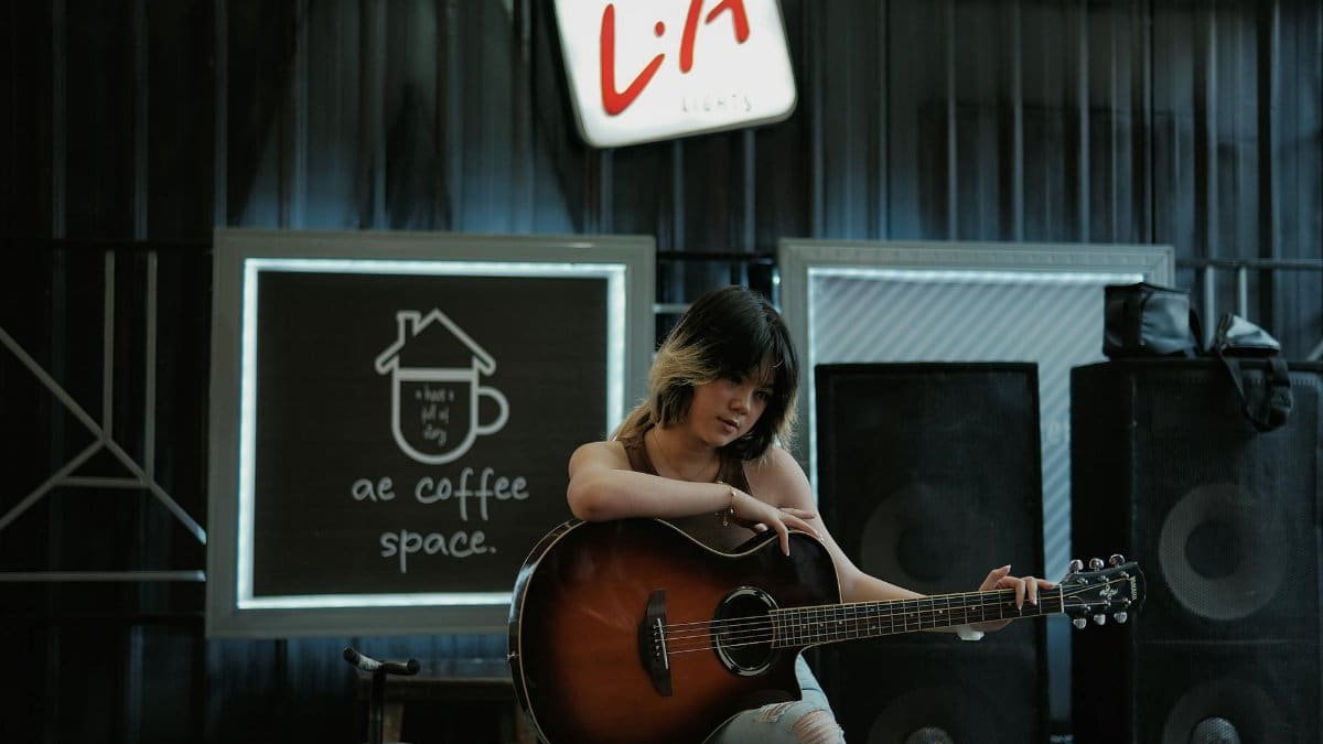 Asian woman playing guitar in a stylish indoor coffee space, showcasing musical passion.