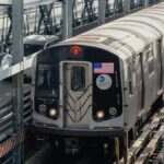 A New York City subway train travels on elevated tracks on a sunny day.