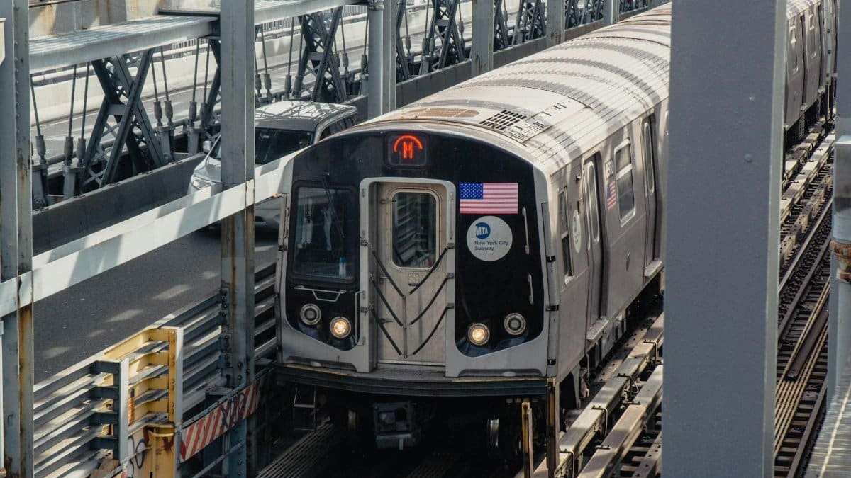A New York City subway train travels on elevated tracks on a sunny day.