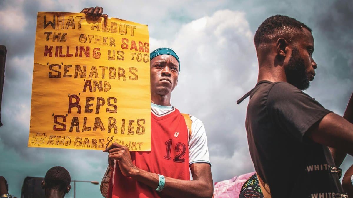 A man holding a protest sign against SARS in a public demonstration under cloudy skies.