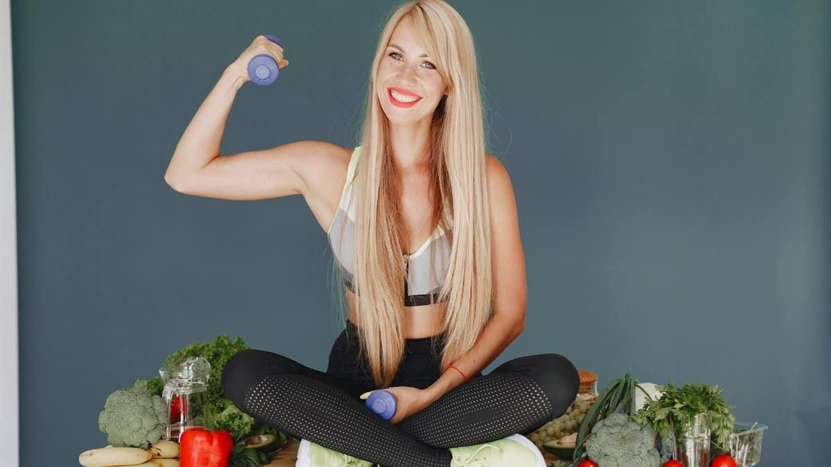 Woman lifting a small dumbbell while surrounded by fresh vegetables, embodying health and fitness.