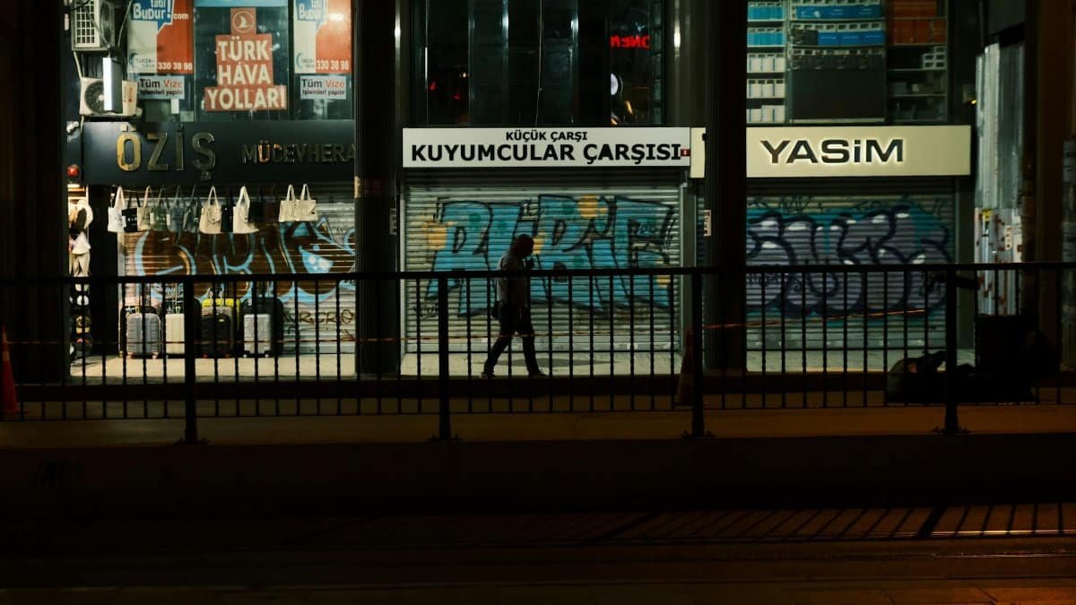 Silhouette of a person walking past graffiti-covered storefronts at night.