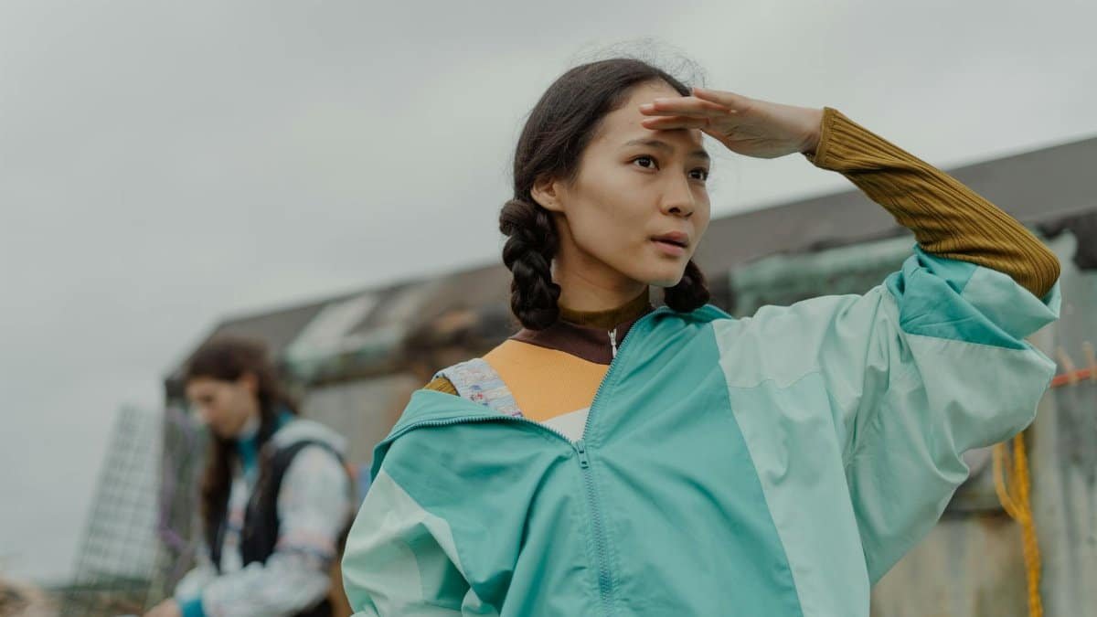 Young woman with braided hair in blue jacket looking into distance outdoors.