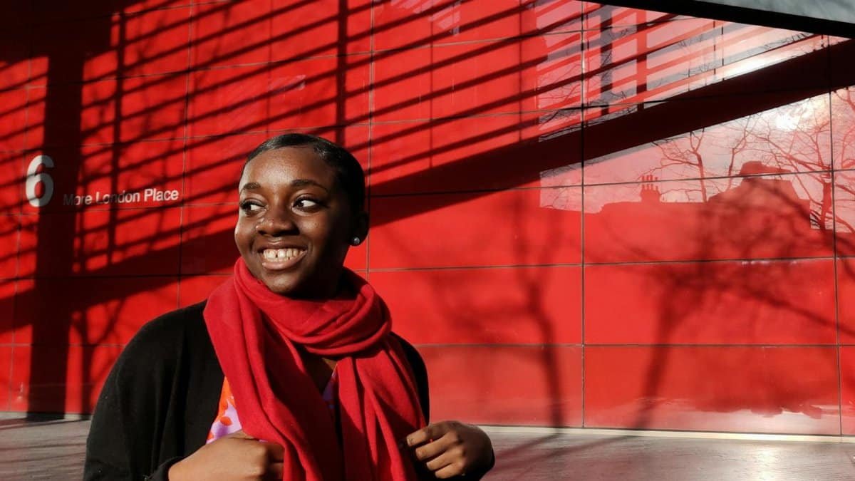 Happy woman wearing a red scarf smiles brightly at More London Place.