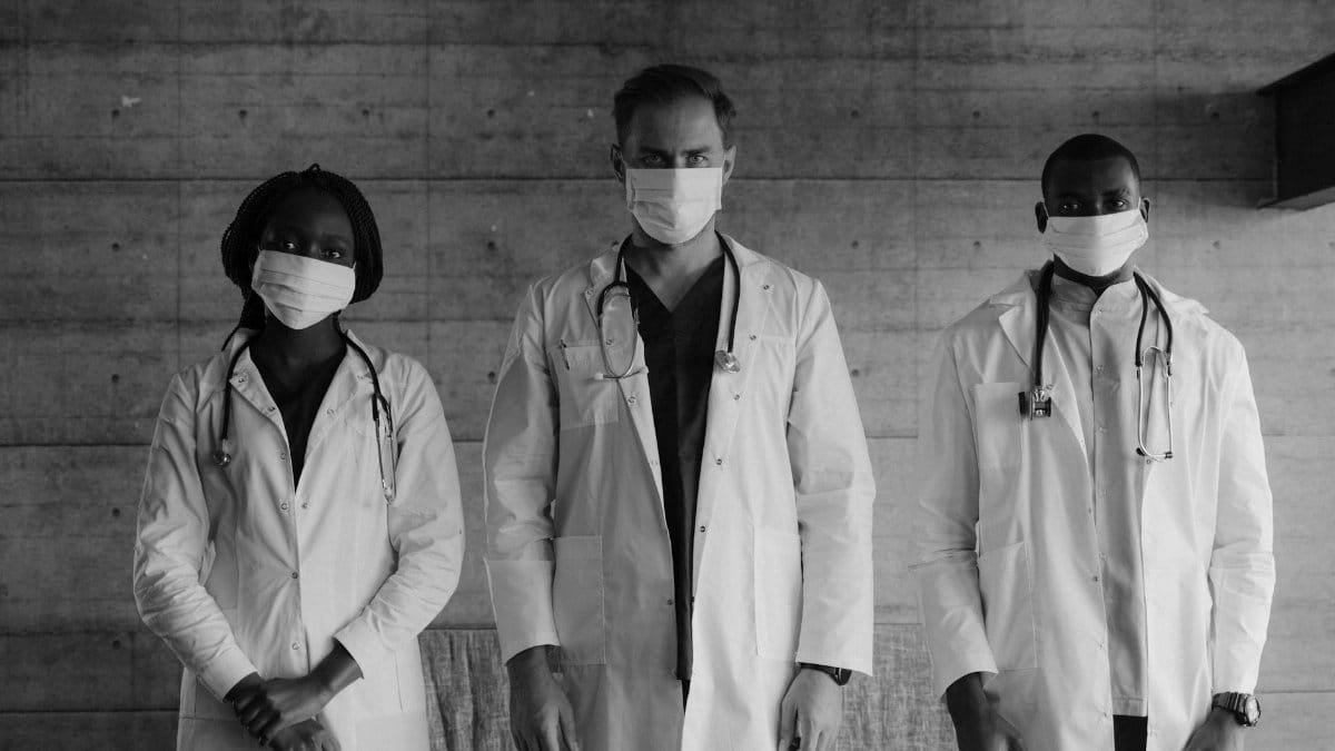 Black and white photo of three healthcare workers wearing masks and stethoscopes indoors.