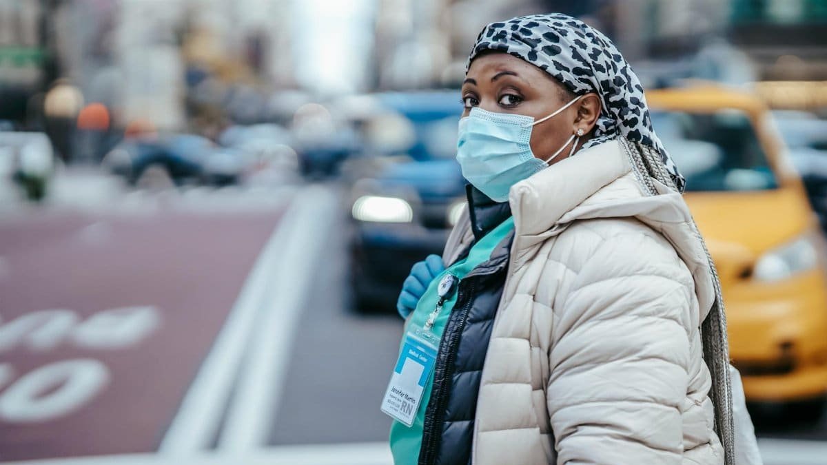 Side view of mature black female medic in outerwear with badge looking at camera on urban roadway