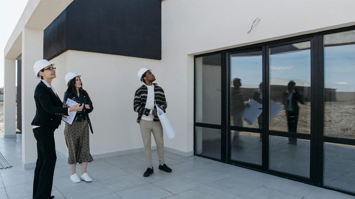 Architects in hard hats discuss the structure of a new building with large glass doors, suggesting a modern architectural design.