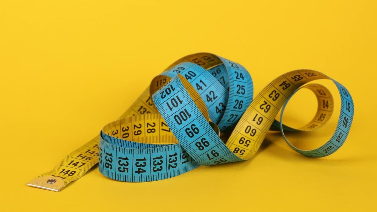 A close-up of a colorful measuring tape curled on a vibrant yellow background.