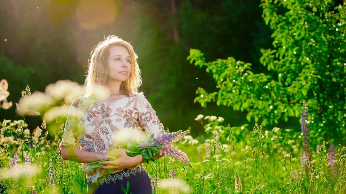 A woman enjoys the sunshine in a lush flower field, holding wildflowers.