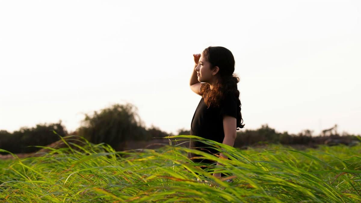 Young girl in a green field looking into the distance under a clear sky, enjoying nature.