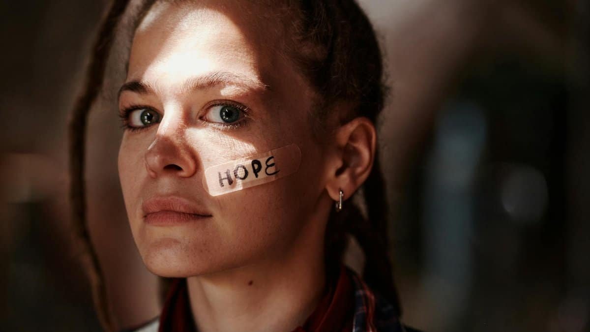 Close-up portrait of a woman with 'hope' written on a band aid. Depicts resilience and optimism.
