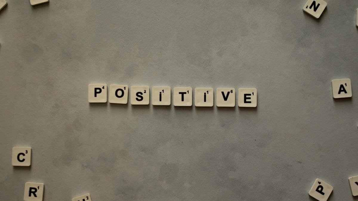 Scrabble tiles arranged to spell 'positive' on a gray textured surface, conveying optimism.