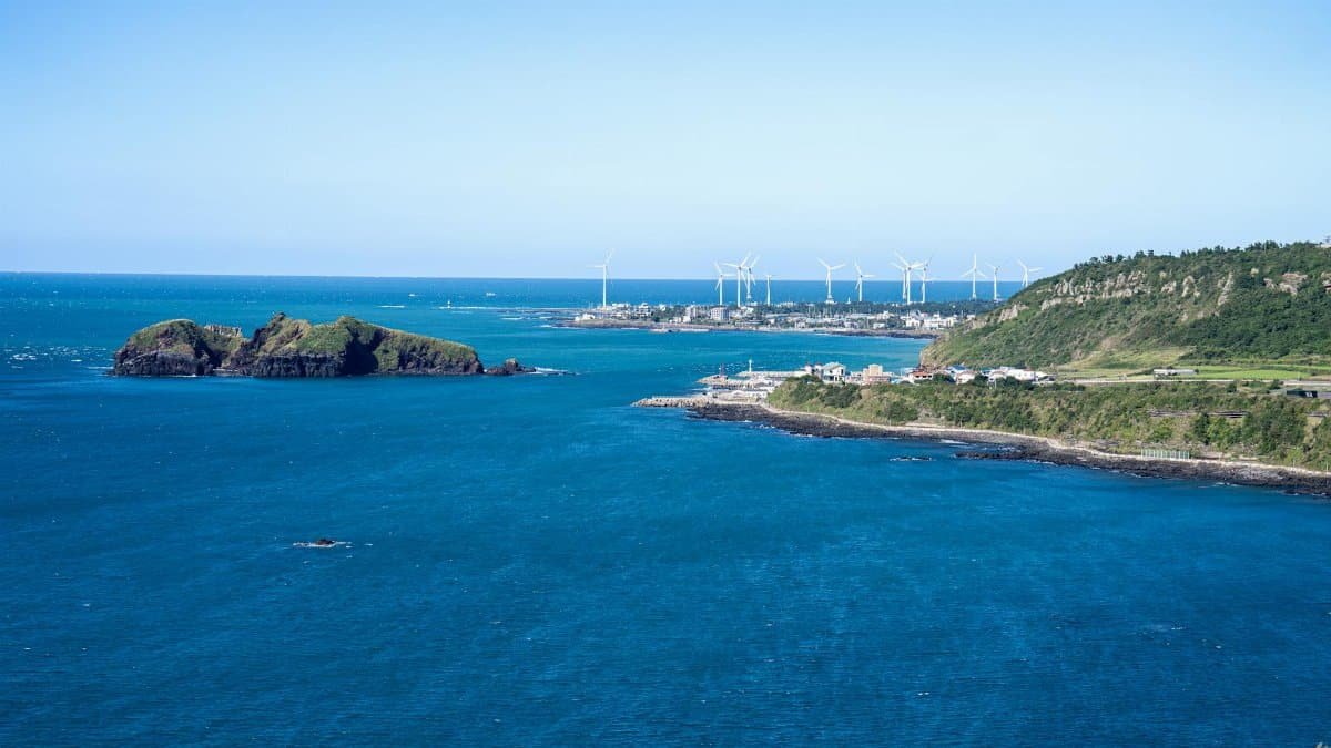 Scenic view of Jeju Island coastline with wind turbines under clear blue skies.