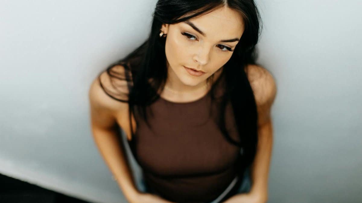 Portrait of a stylish woman in a brown tank top leaning against a wall, looking thoughtful.