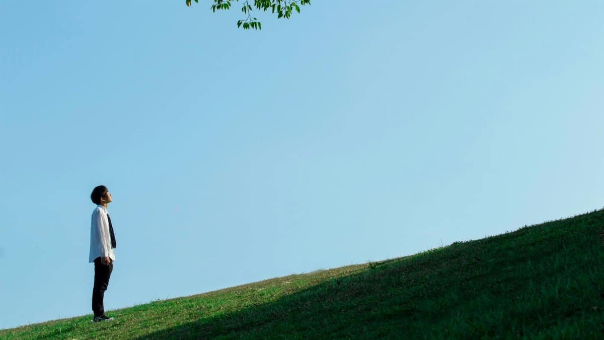 Adult male looking up while standing on a grassy hill under a clear sky.