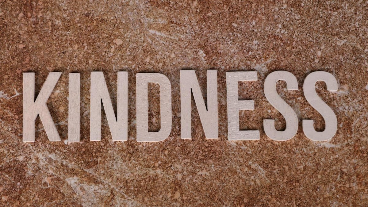 Wooden letters spelling 'Kindness' on a textured stone background, conveying a positive message.