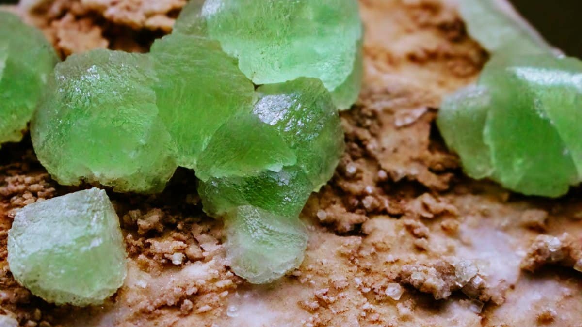 Close-up of bright green crystals on a textured mineral surface, showcasing natural beauty.