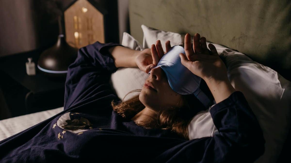 A woman in comfortable attire rests indoors wearing a sleep mask, exuding a cozy and peaceful mood.