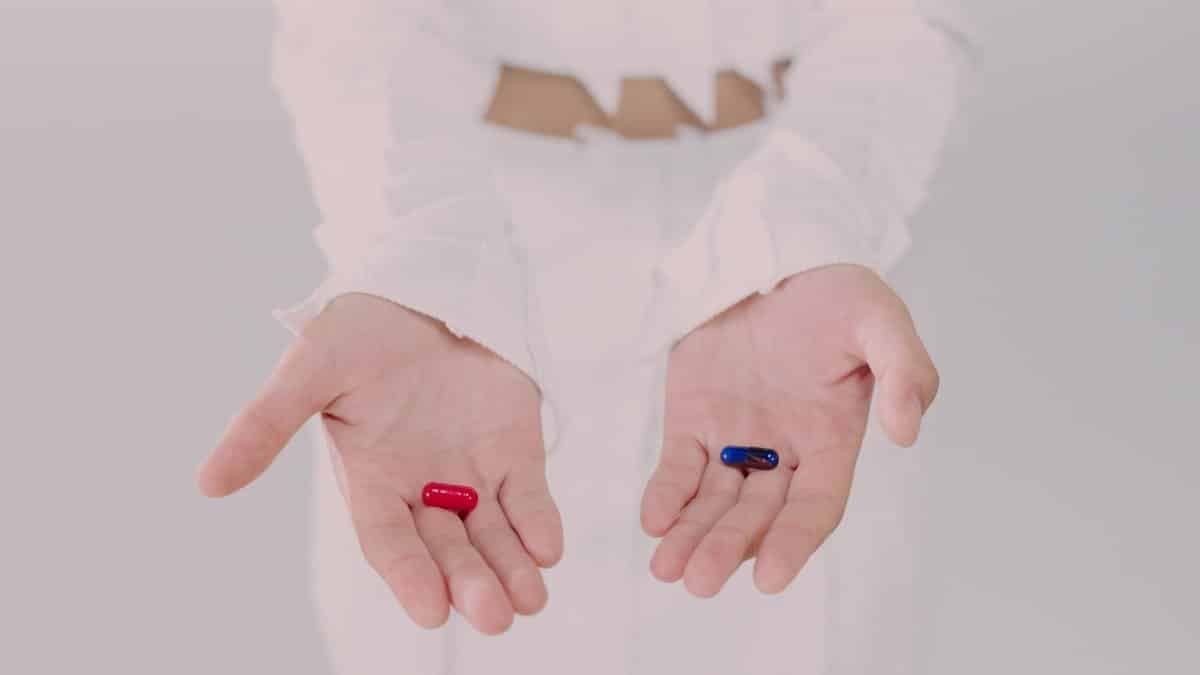 Close-up of hands holding red and blue pills, symbolizing a choice. Conceptual studio shot.