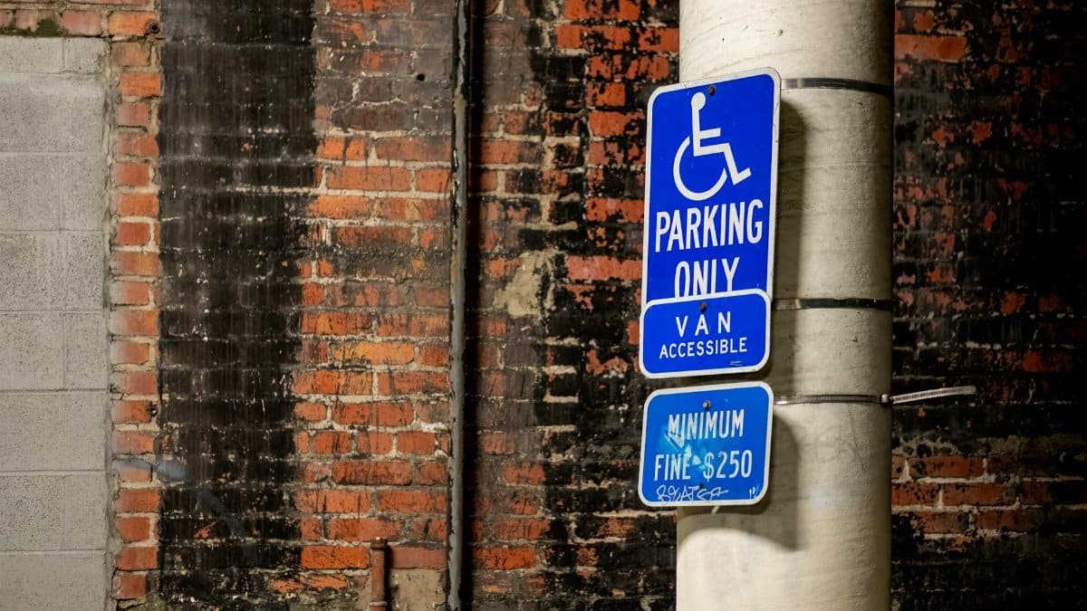 Blue handicap parking sign attached to a pole against a brick wall in the city.
