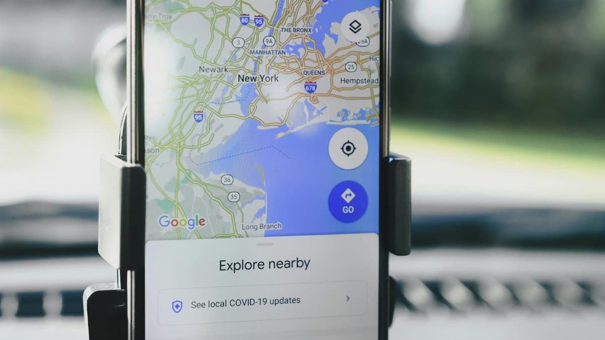 A smartphone displaying GPS map of New York City secured in a car mount during daylight.