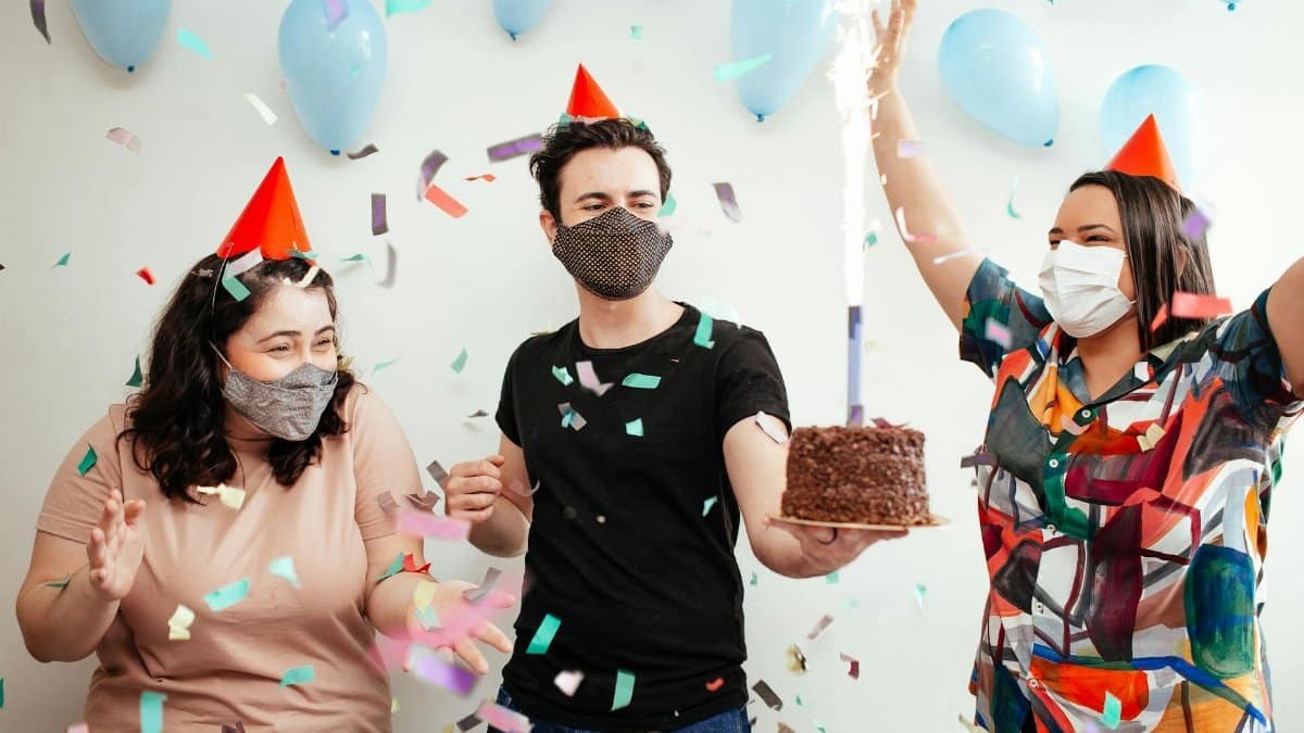 Joyful birthday party with friends indoors, wearing masks, and enjoying cake and confetti.