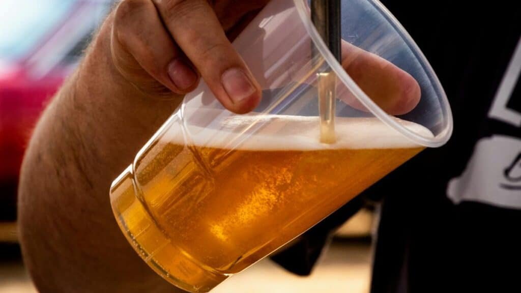 Close-up of a person pouring golden craft beer into a clear plastic cup.