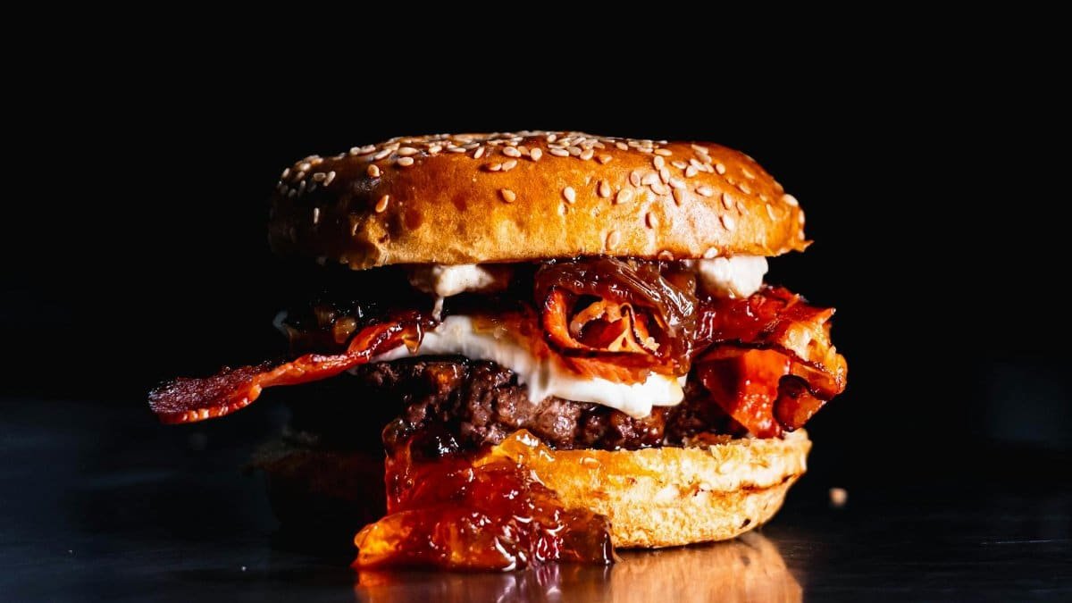 Close-up of a gourmet burger featuring bacon and sauce in vivid detail.