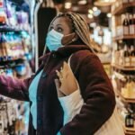 Side view of African American female shopper in protective mask and gloves selecting goods in grocery store