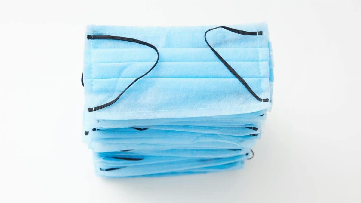 Close-up image of a stack of blue surgical face masks with earloops on a white background, ideal for medical themes.