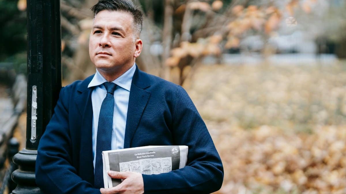 A confident businessman in formal attire stands outdoors holding a newspaper, exuding professionalism.