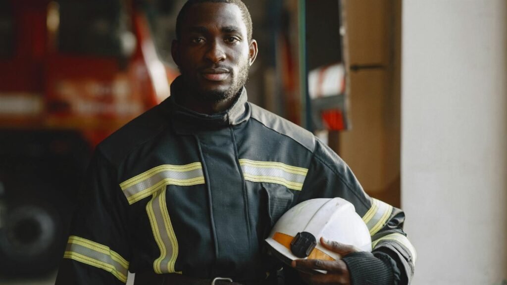 Black firefighter in uniform holding helmet, showcasing professionalism.