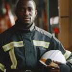 Black firefighter in uniform holding helmet, showcasing professionalism.