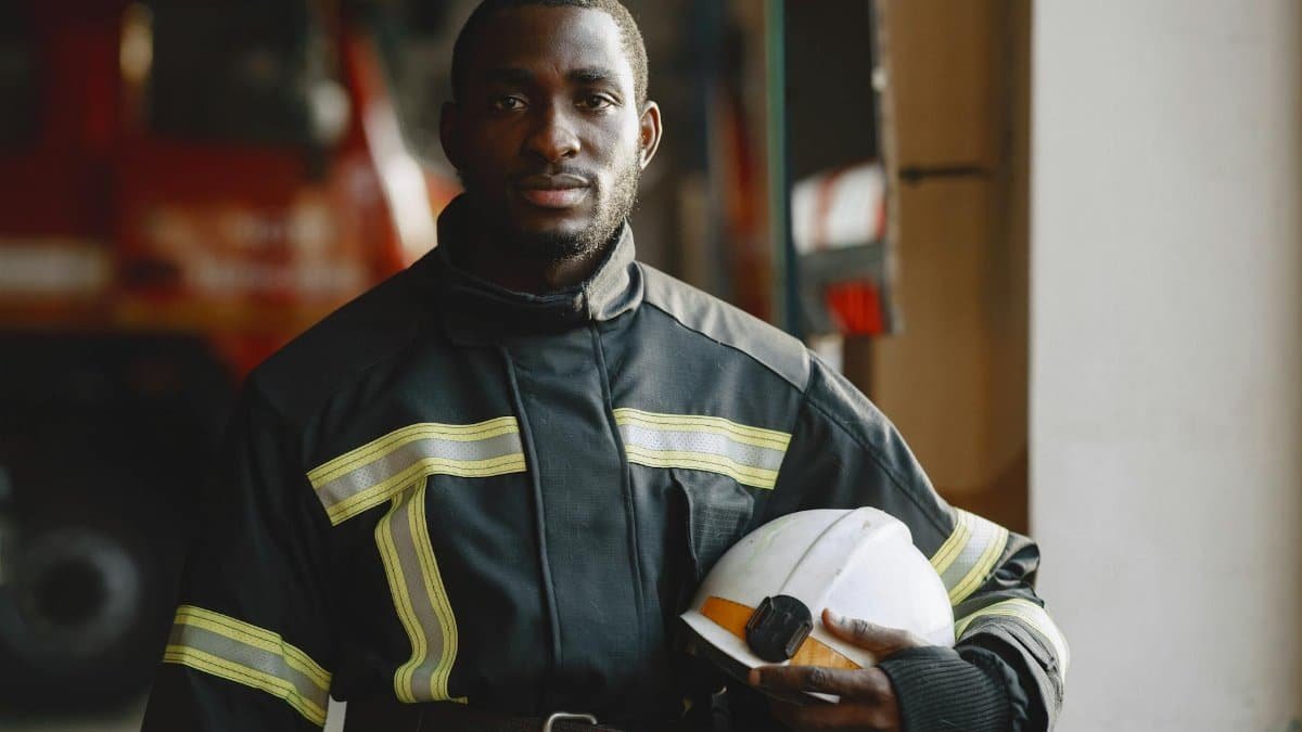 Black firefighter in uniform holding helmet, showcasing professionalism.