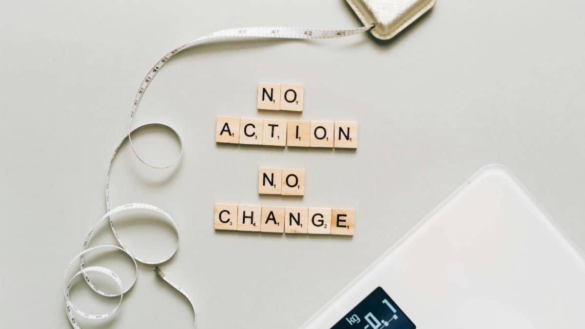 Motivational concept with scrabble tiles spelling no action no change alongside a measuring tape and scale.