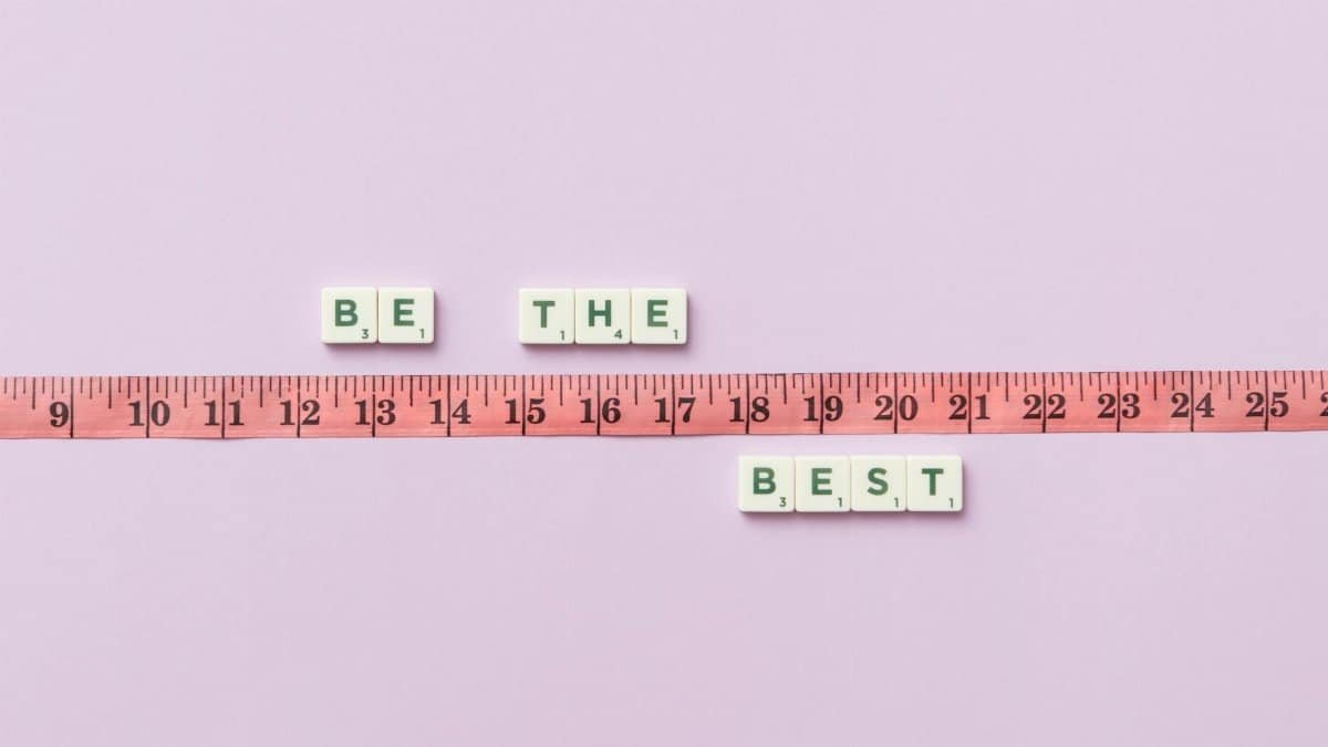 Scrabble tiles spell 'Be the Best' next to a measuring tape on a pastel background.