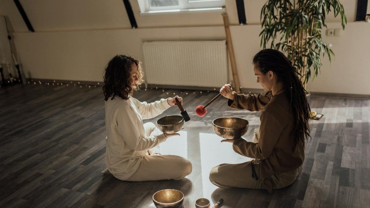 Two women sitting and meditating with Tibetan singing bowls indoors, creating a serene atmosphere.