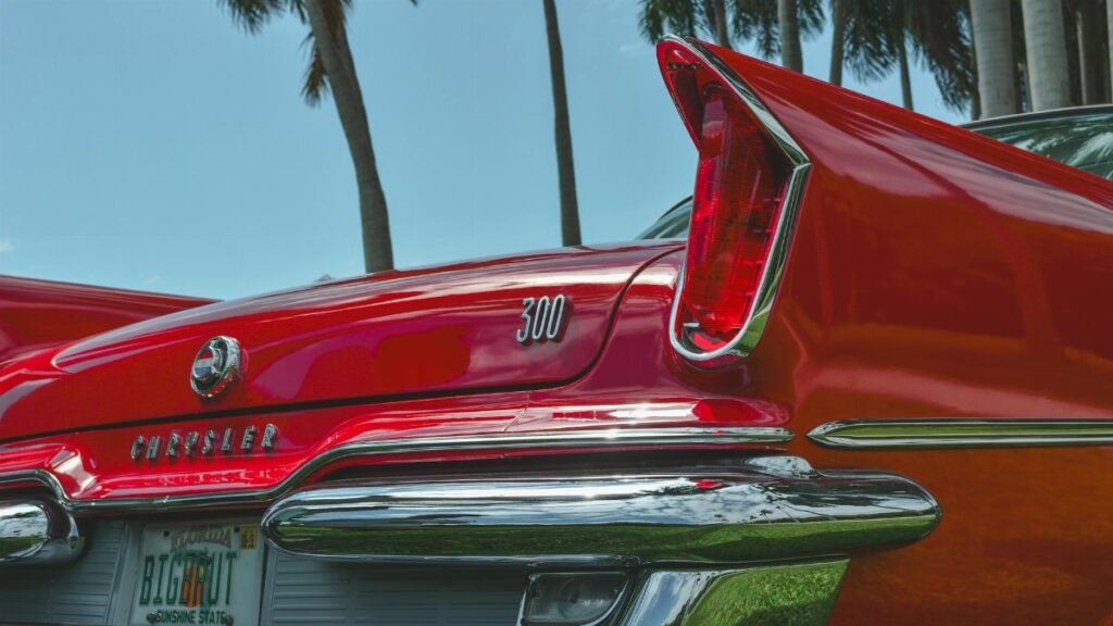 Vintage Chrysler 300 in red with palm trees, showcasing classic tail fin design with a sunny backdrop.