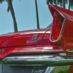 Vintage Chrysler 300 in red with palm trees, showcasing classic tail fin design with a sunny backdrop.