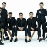 A stylish group of men in suits posing elegantly against a white backdrop in a studio setting.