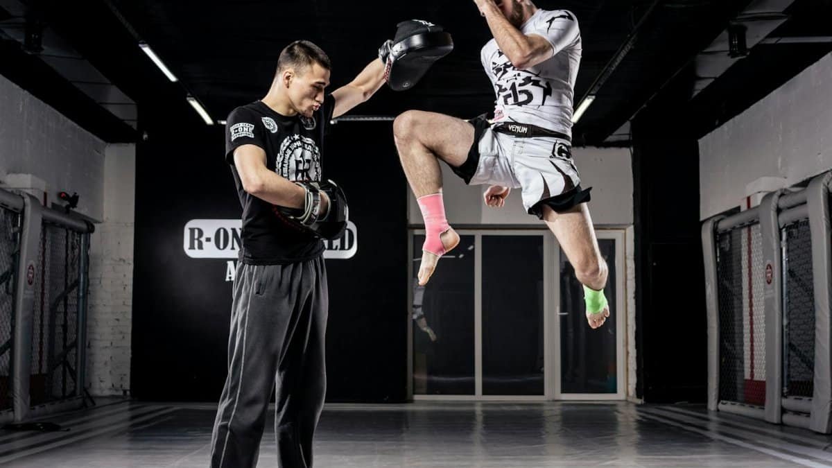 Two men practicing martial arts in a gym, showcasing a high kick and focus on training.