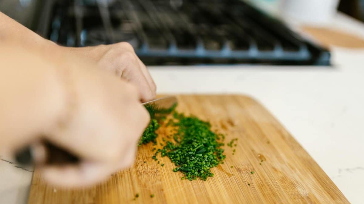 Hands chopping fresh chives on a wooden cutting board in a kitchen setting. Perfect for culinary content.