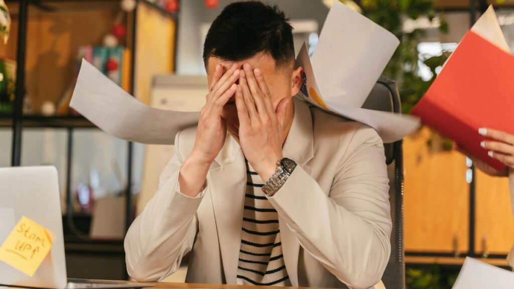 Stressed businessman overwhelmed by paperwork in office environment, demonstrating burnout.
